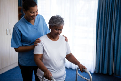 Nurse hepling senior women in walking with walker at nursing home