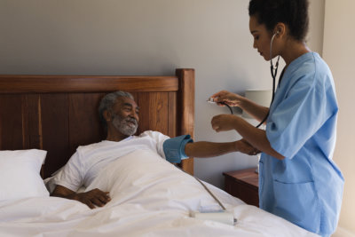 doctor measuring blood pressure of senior man in bedroom at home